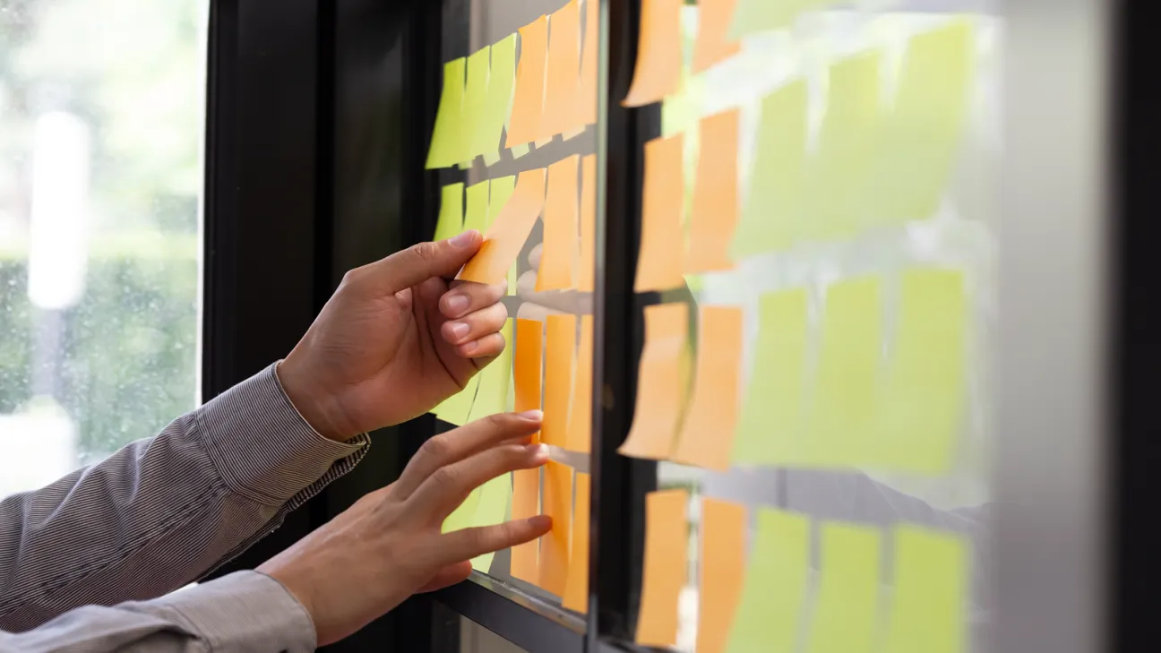 Yellow and orange post it notes being applied to a wall by a person